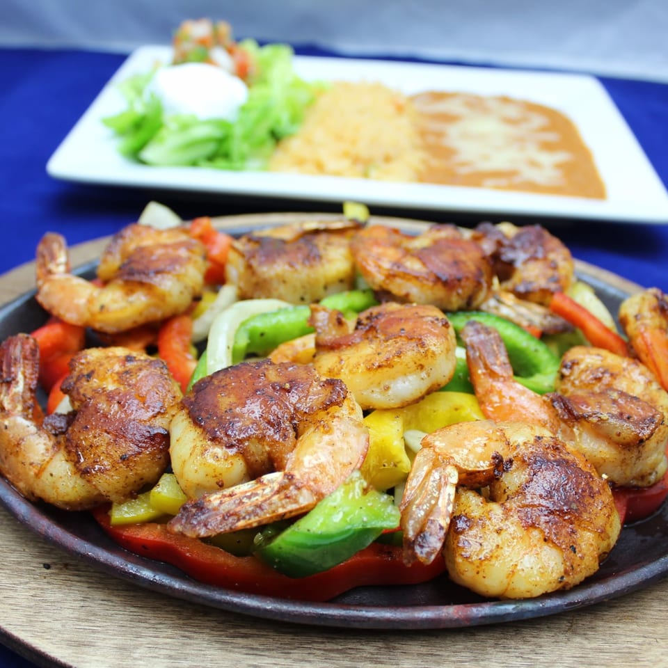 Sizzling shrimp fajitas with colorful bell peppers and onions, with rice and beans in the background.