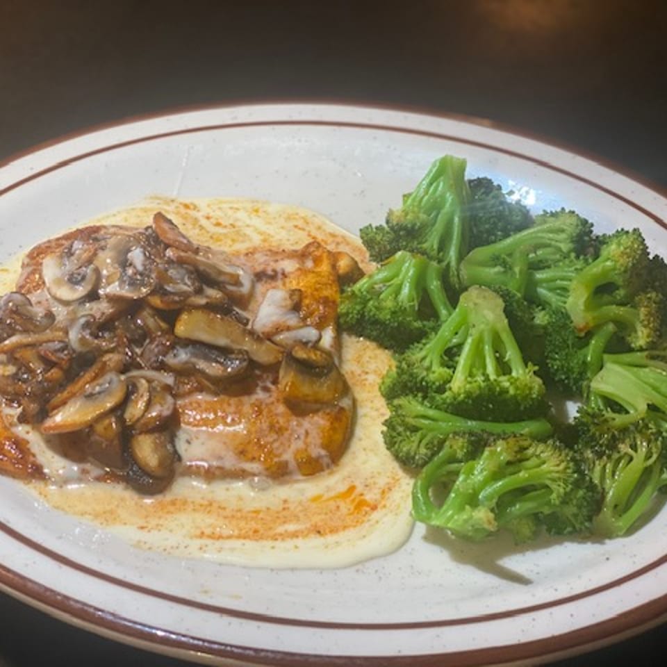 Chicken breast with creamy mushroom sauce and a side of steamed broccoli on a white plate.